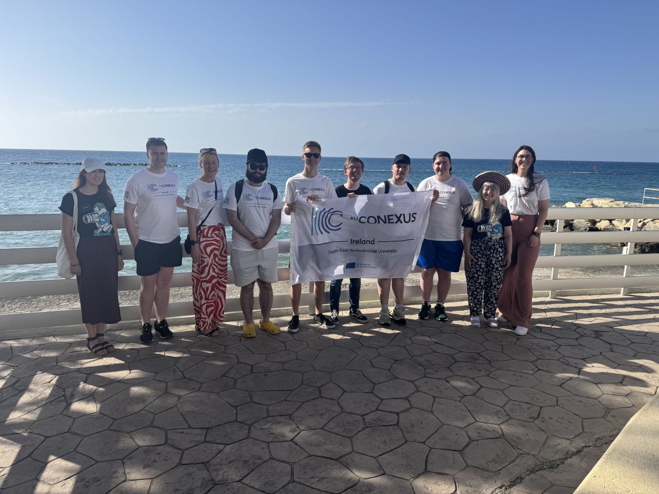 Group of students holding the EU-CONEXUS flag. Sea in the background