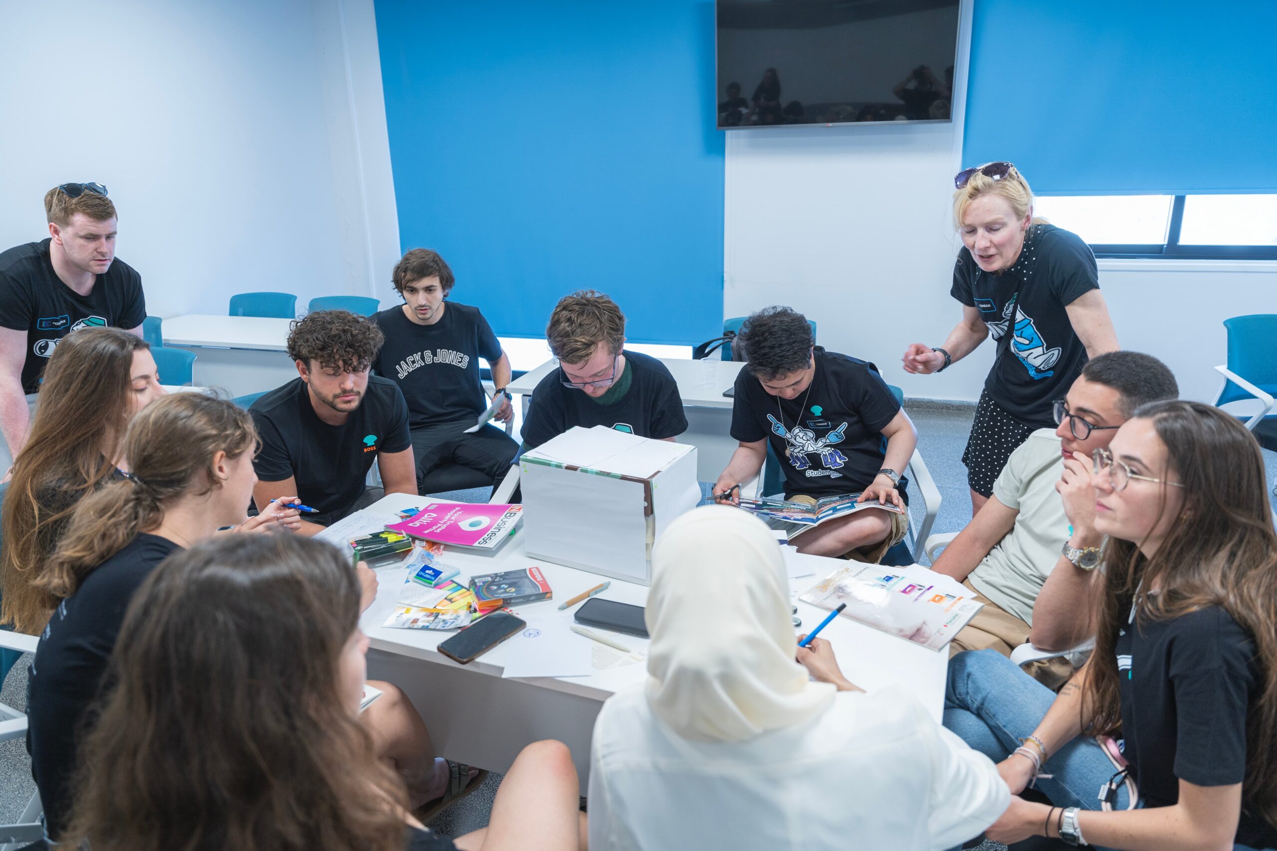 Group of students working around a table. Magazines and markers